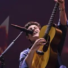 Shawn Mendes śpiewa i gra na gitarze na koncercie.