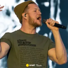 Wokalista Imagine Dragons śpiewa do mikrofonu, ubrany w zieloną koszulkę i czapkę.