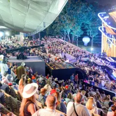 Tłumy widzów na amfiteatralnych trybunach podczas festiwalu w Opolu. Na scenie widowiskowe oświetlenie i dekoracje.