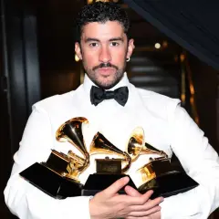 Bad Bunny, ubrany w białą koszulę i czarną muszkę, trzyma kilka złotych nagród Grammy.