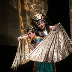 Dwie kobiety w złotych, skrzydlatych strojach na scenie opery Aida.