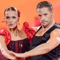 Para tańczy w strojach inspirowanych folklorem. Kobieta w czerwonej sukni z falbankami, mężczyzna w czarnej kamizelce.