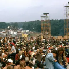 Tłum ludzi na festiwalu, widoczne wieże z głośnikami i scena w tle.