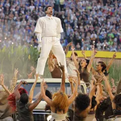Bad Bunny na Super Bowl, otoczony przez tancerzy i tłum, na tle kukurydzy i stadionu.
