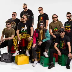 Dziewięciu mężczyzn w okularach przeciwsłonecznych, ubranych w koszulki z motywami reggae, siedzi na skrzynkach po napojach.