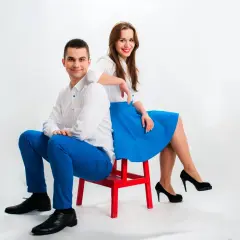 Mężczyzna i kobieta siedzą na czerwonym krześle, ubrani na biało i niebiesko.