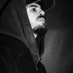 Czarno-białe zdjęcie Taco Hemingwaya w bluzie z kapturem i czapce, patrzącego w bok.