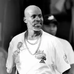 DMX w białej koszulce z łańcuchem na szyi, z tatuażem "EXODUS" na karku, uśmiecha się podczas występu.