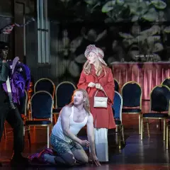 Aktorzy na scenie operetki, mężczyzna klęczy, kobieta stoi, trzeci mężczyzna trzyma kostium.