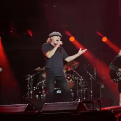 Zespół AC/DC na scenie, wokalista śpiewa, gitarzyści grają. Czerwone światła.