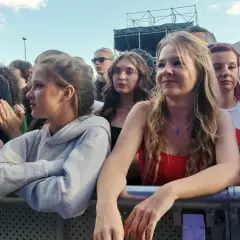 Uśmiechnięci ludzie na koncercie podczas Dni Sosnowca. Widać fragmenty sceny i tłum bawiący się przy muzyce.