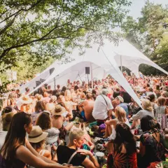 Tłum ludzi siedzi pod białym namiotem na festiwalu Wibracje, słuchając wystąpienia.