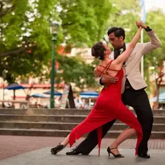 Para tańczy tango na zewnątrz, kobieta w czerwonej sukience, mężczyzna w jasnej marynarce.