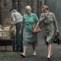 Kobiety idą obok wózka z workami, jedna z nich kicha. Scena z serialu "Ołowiane dzieci".
