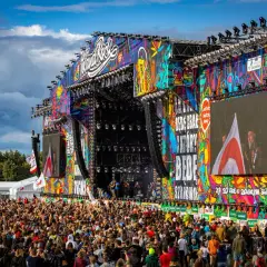 Kolorowa scena festiwalu polandrock 2026 z tłumem fanów. Na ekranach widać artystów, a nad nimi tęczowe grafiki.