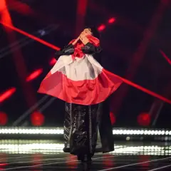 Eurowizja zwycięzcy: artysta w czarnym stroju z biało-czerwoną flagą na scenie, otoczony czerwonymi światłami.