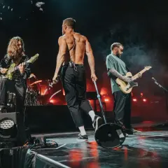 Imagine Dragons na koncercie w Polsce: wokalista bez koszulki, gitarzyści grający na scenie.
