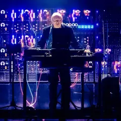 Hans Zimmer stoi przy syntezatorze na tle ściany pełnej migających świateł i kabli.