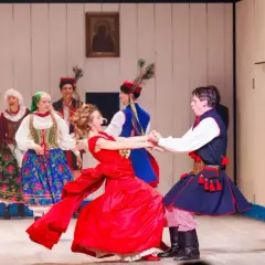 Aktorzy w strojach ludowych tańczą na scenie.