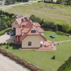 Piękny dom z ogrodem, gdzie mieszka Skolim. Widać panele słoneczne, dwa samochody i plac zabaw.