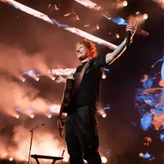 Ed Sheeran na koncercie w Polsce, grając na gitarze i pozdrawiając publiczność.