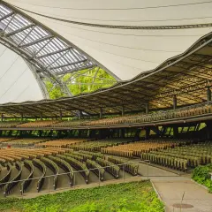Amfiteatr z rzędami pustych siedzeń pod zadaszeniem, otoczony zielenią.