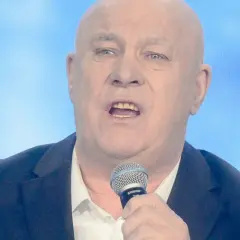 Ryszard Rynkowski śpiewa do mikrofonu, ubrany w marynarkę i białą koszulę.