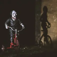 Figurka Billy'ego z horroru 2023 na czerwonym rowerku trójkołowym, rzucająca złowieszczy cień.