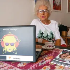 Starsza kobieta w okularach siedzi przy laptopie z grafiką DJ Wika.