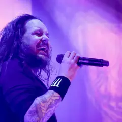 Jonathan Davis z zespołu Korn śpiewający do mikrofonu na fioletowej scenie.