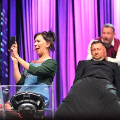 Trzech aktorów na scenie: kobieta robi selfie, mężczyzna w sutannie i drugi mężczyzna za nim.