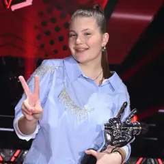 Dziewczynka w błękitnej koszuli z kryształkami, trzymająca statuetkę i pokazująca znak V.
