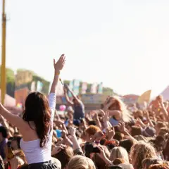 Tłum ludzi na festiwalu muzycznym, z rękami w górze, w tle namioty i sceny.