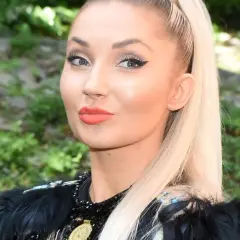 Cleo, której wiek dodaje jej uroku, w czarnej, ozdobnej kreacji z piórami.