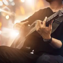 Mężczyzna grający na gitarze akustycznej na tle rozmytych świateł.