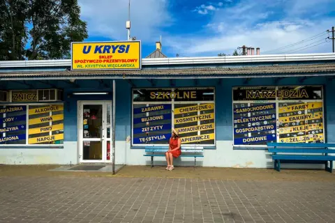 Dziewczyna w czerwonej sukience siedzi na ławce przed sklepem "U Krysia", gdzie kręcono "Ranczo".
