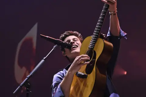 Shawn Mendes śpiewa i gra na gitarze na koncercie.
