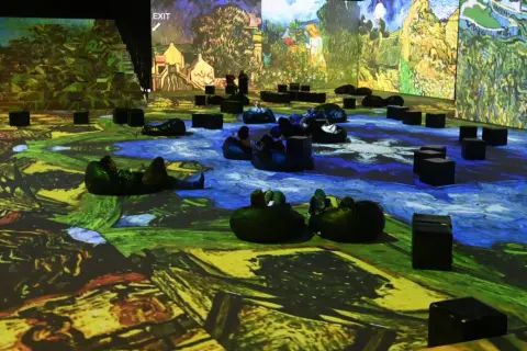 Wystawa Van Gogh w Krakowie. Widzowie odpoczywają na pufach, otoczeni projekcjami dzieł mistrza.