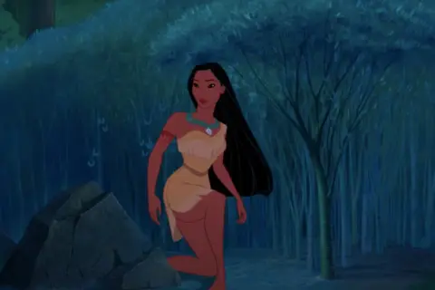 Pocahontas, jedna z księżniczek Disneya, klęczy w mrocznym lesie obok skały.