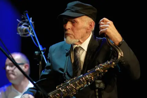 Jan Ptaszyn Wróblewski, legendarny saksofonista, w czapce i garniturze, trzymający saksofon.