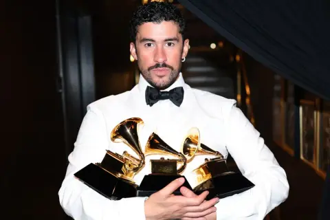 Bad Bunny, ubrany w białą koszulę i czarną muszkę, trzyma kilka złotych nagród Grammy.