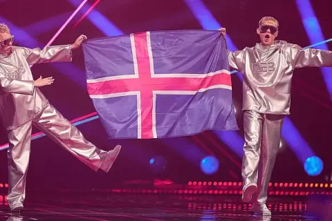 Dwóch artystów w srebrnych strojach prezentuje flagę Islandii na scenie Eurowizji.