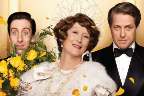Meryl Streep w koronie i perłach, obok Hugh Granta i Simona Helberga, w scenie z jednego z jej filmów.