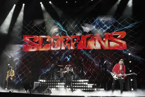 Zespół Scorpions na scenie z dużym logo zespołu i efektami świetlnymi.