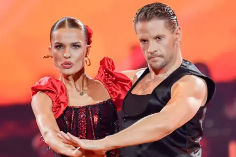 Para tańczy w strojach inspirowanych folklorem. Kobieta w czerwonej sukni z falbankami, mężczyzna w czarnej kamizelce.