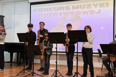 Młodzi muzycy grają na instrumentach: skrzypcach, saksofonach i gitarach, na tle ekranu z napisem "Konkurs Muzyki Rozrywkowej".