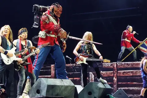 Zespół Iron Maiden na scenie, w tym Eddie w czerwonym mundurze, grający na gitarach i z flagą Wielkiej Brytanii.