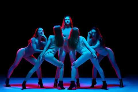 Pięć kobiet w body i butach na obcasach wykonuje zmysłowy taniec high heels w neonowym świetle.