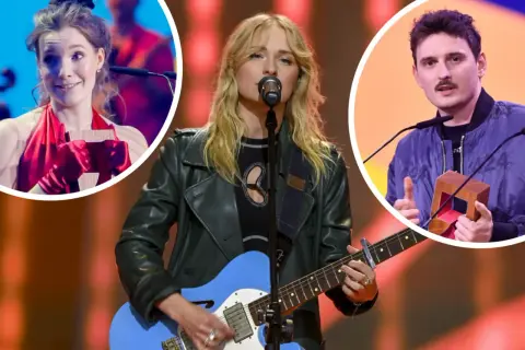 Trzy osoby na scenie: kobieta gra na gitarze, kobieta w czerwieni trzyma nagrodę, mężczyzna z wąsami trzyma nagrodę.
