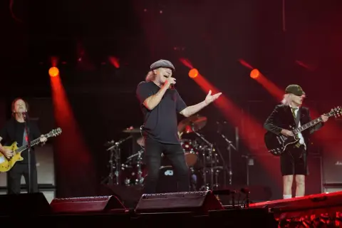 Zespół AC/DC na scenie, wokalista śpiewa, gitarzyści grają. Czerwone światła.